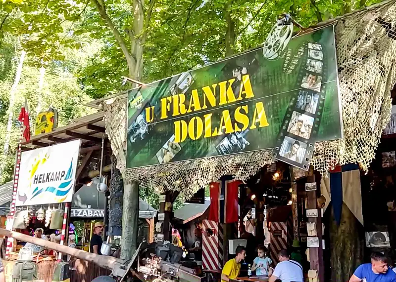 Zielony szyld U Franka Dolasa nad wejściem, wokół drzewa